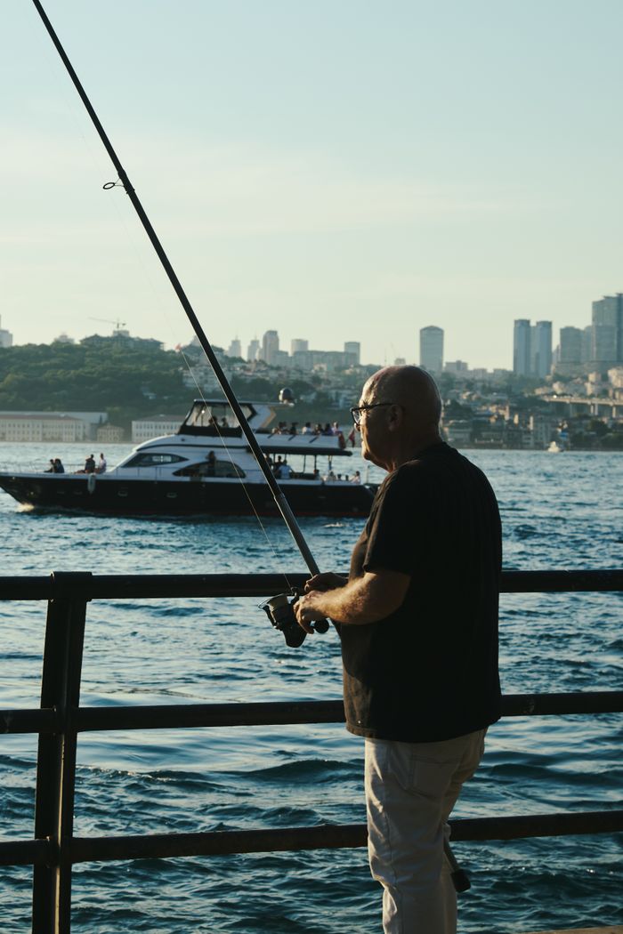 A man fishes by the Bosphorus Strait with a cityscape in the background, showcasing Istanbul's coastal charm.
